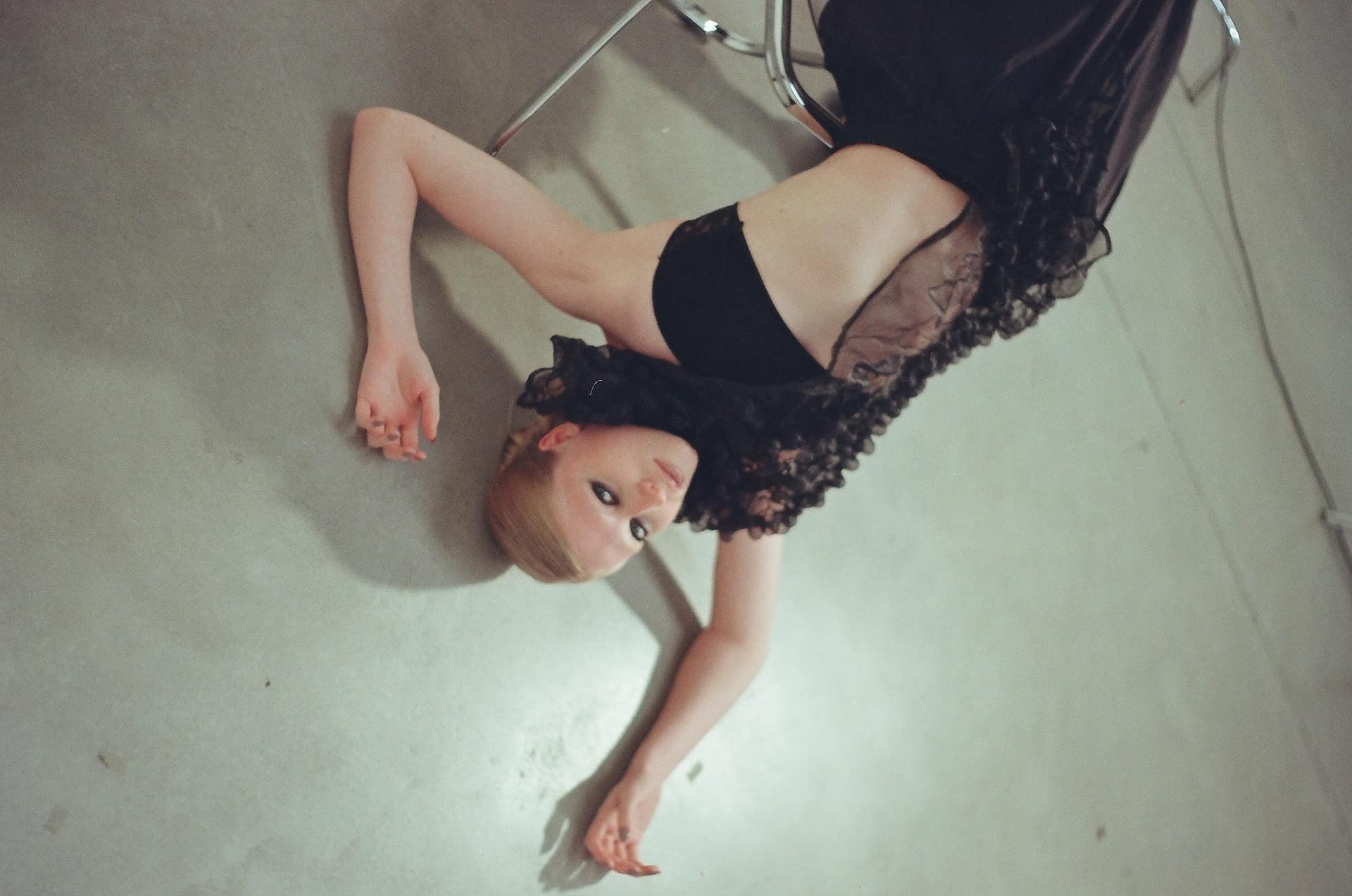 Modelo con vestido negro recostada en el piso de hormigón