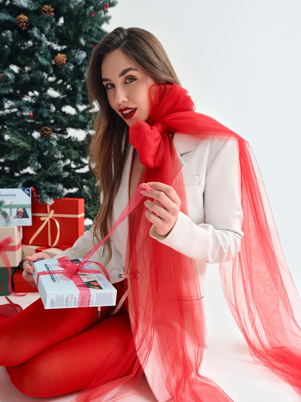 Producción navideña de Anua: modelo con pañuelo rojo junto al árbol con regalos